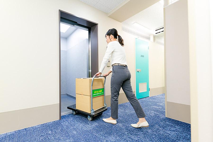 女性が荷物を乗せた台車を押してエレベーターに入る様子